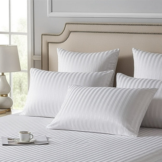 A neatly made bed with white Egyptian cotton striped bedding and pillows on a cream bed frame and headboard.
