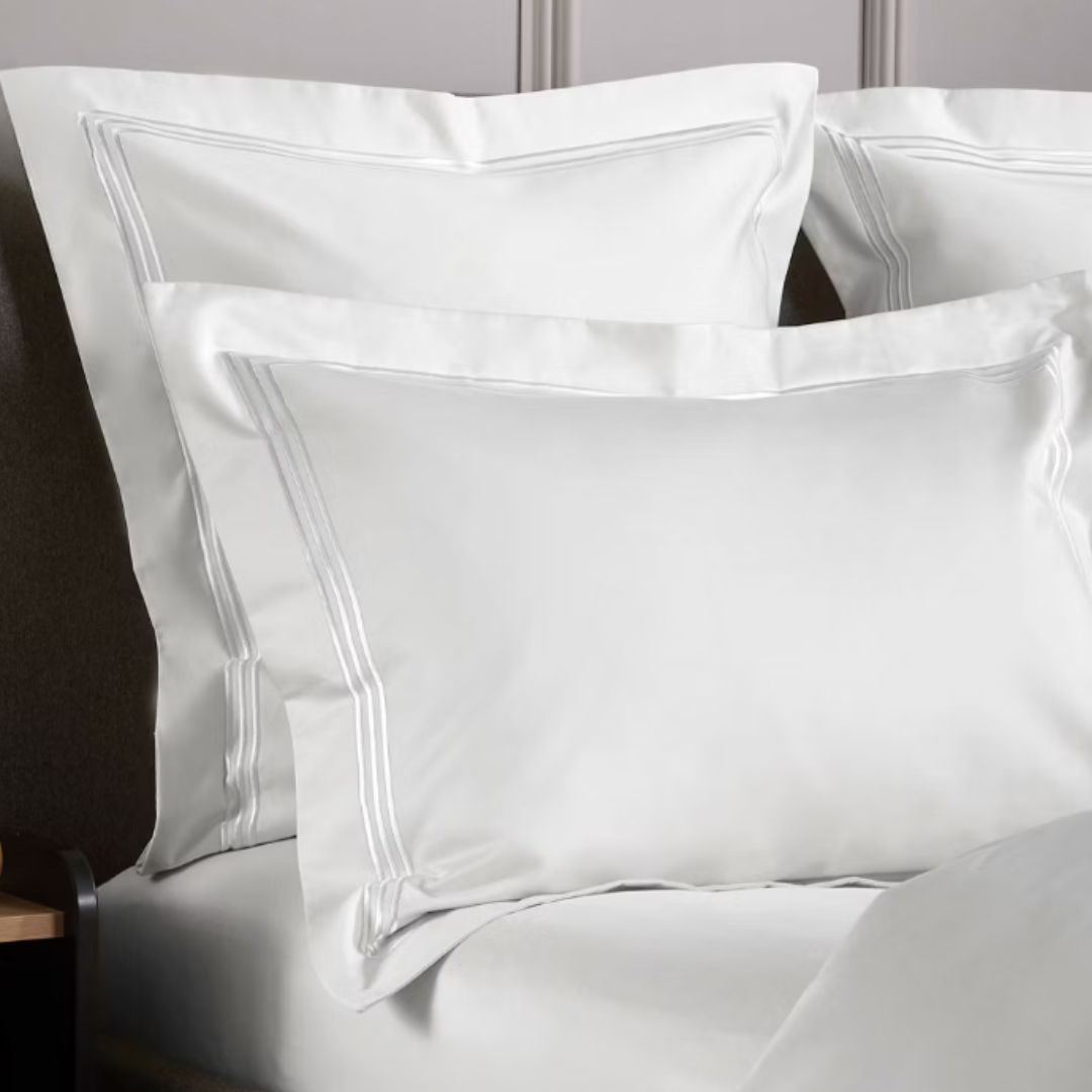 Close-up of white satin pillows on a bed with a neutral background