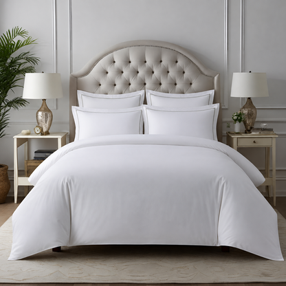 A neatly made bed with crisp white bedding, including a duvet cover and four matching pillows, set against a beige tufted headboard in a styled bedroom with matching nightstands, lamps, and a plant.