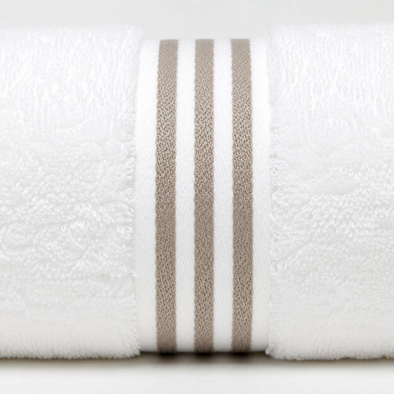 A close-up of a white textured towel roll with three vertical taupe-beige stripes on a light gray background.
