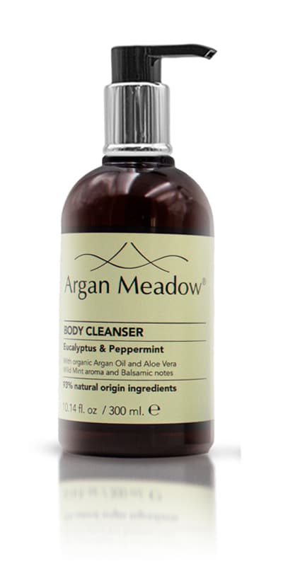 A pump bottle of Argan Meadow hair wash placed on a rocky surface with a body of water in the background.