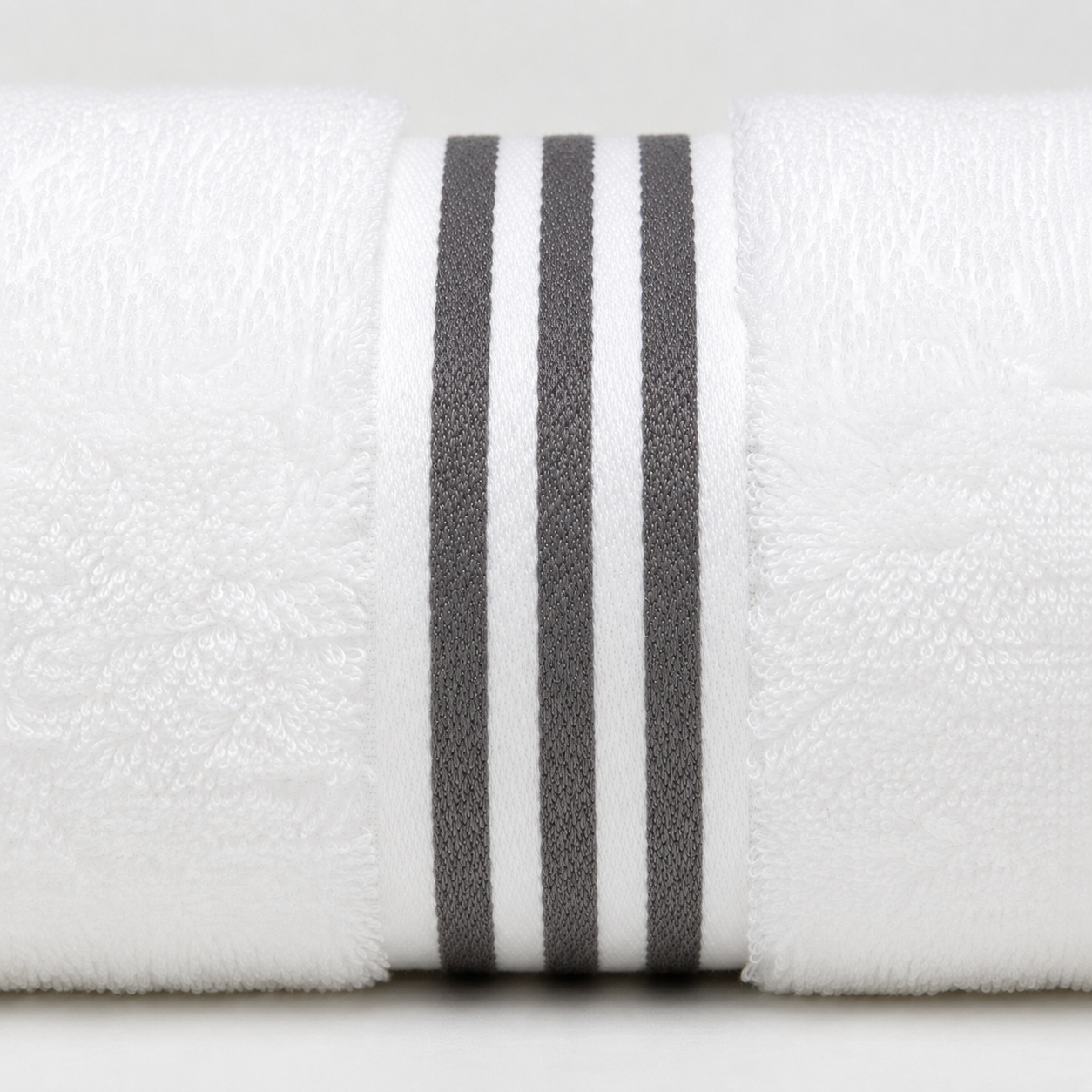 A close-up of a white textured towel roll with three vertical dark gray stripes near the center, photographed against a light neutral background.