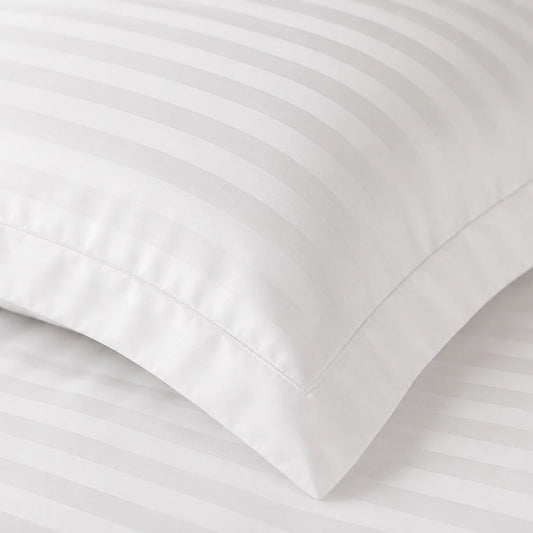A close-up of a white pillowcase with matching striped bedding, showing the corner and folded edge of the fabric.