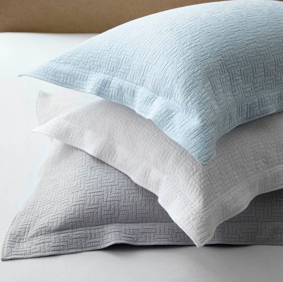 Stack of textured pillows in light blue, gray, and white on a neutral background