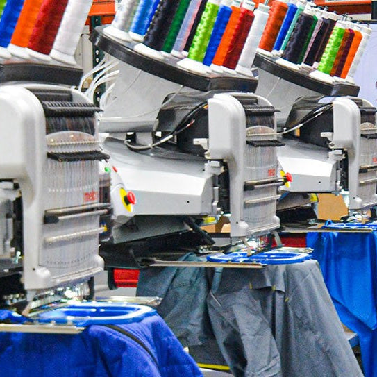 Embroidery machines with colorful threads and fabric in a workshop setting.
