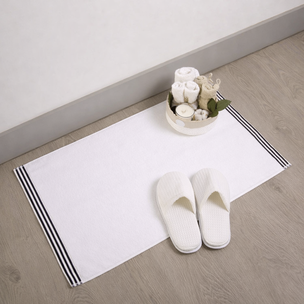 White slippers on a white rug with black stripes, accompanied by a small decorative bowl of flowers on a wooden floor.