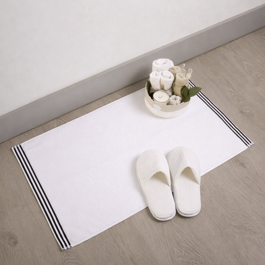 White slippers on a white rug with black stripes, accompanied by a small decorative bowl of flowers on a wooden floor.